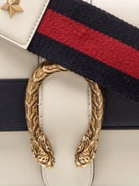 YoloLuxe Handbags off-white leather bag featuring a gold tiger head clasp and a navy and red striped shoulder strap.